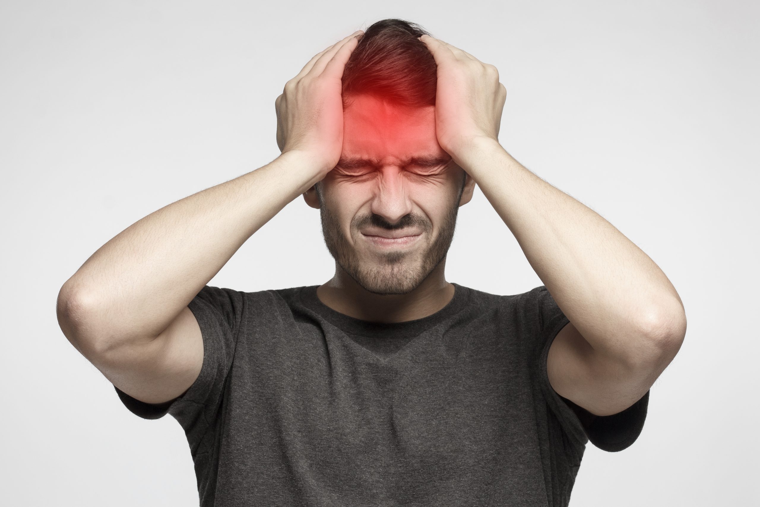 Young man isolated on gray background, showing how much head hurts, experiencing pain, looking miserable and exhausted. Headache concept.